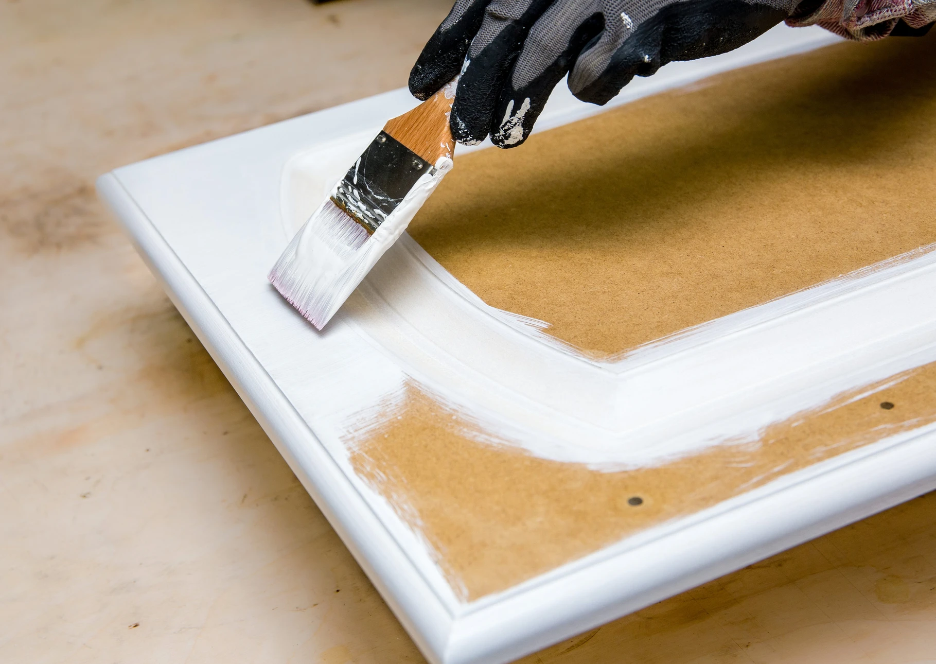 Intérieur atelier peinture avec pot de peinture rose ouvert et pinceau plat à manche blanc posé dessus, sur surface en bois naturel aux veines apparentes