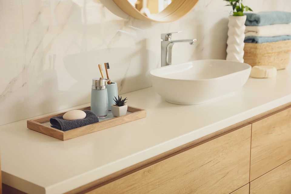 Salle de bain moderne avec vasque blanche posée sur plan de travail en pierre claire et meuble bas en bois naturel