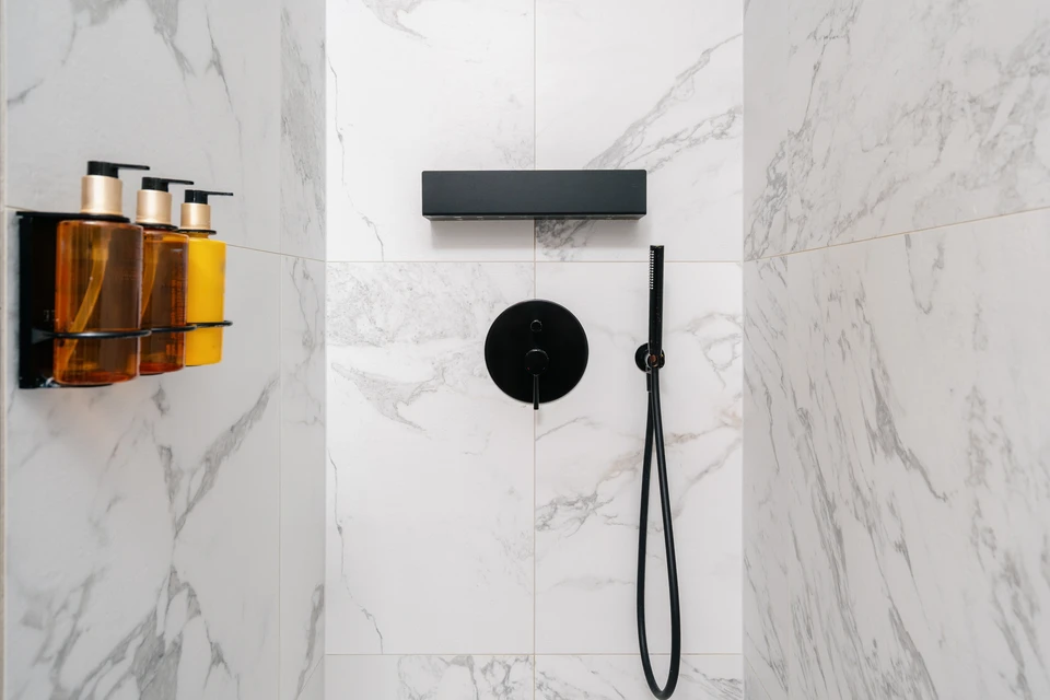 Homme en chemise noire avec ceinture à outils installant un système de douche moderne dans une salle de bain contemporaine aux murs vitrés
