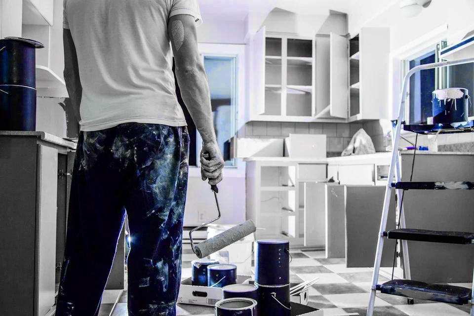 Artisan peintre en bâtiment travaillant dans une cuisine en rénovation, appliquant de la peinture blanche sur les meubles avec un rouleau